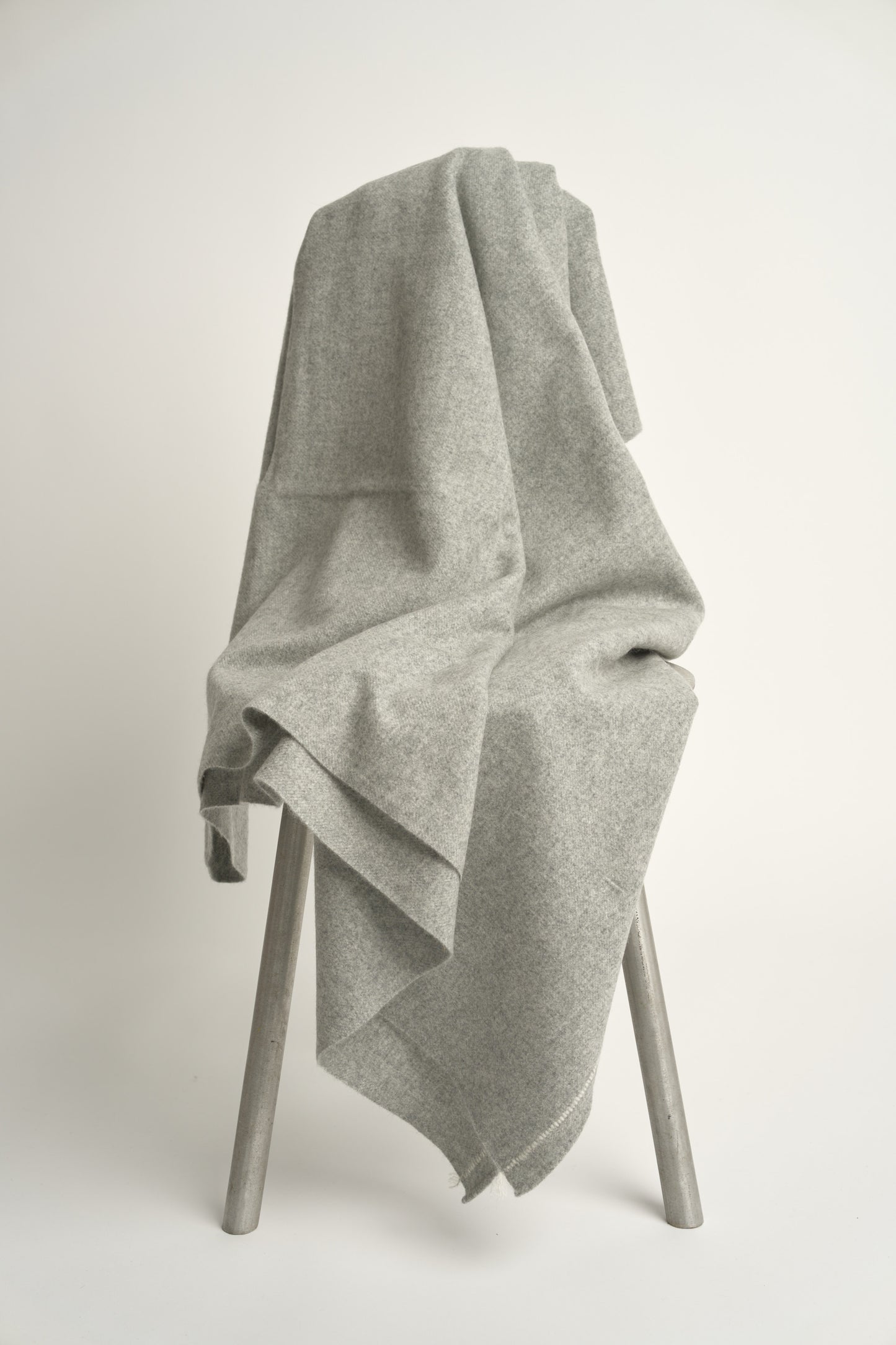 A soft grey throw with hand-rolled edges and a contrast color stitch line; draped over a chair