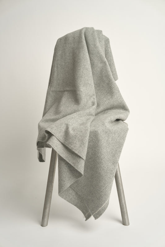 A soft grey throw with hand-rolled edges and a contrast color stitch line; draped over a chair