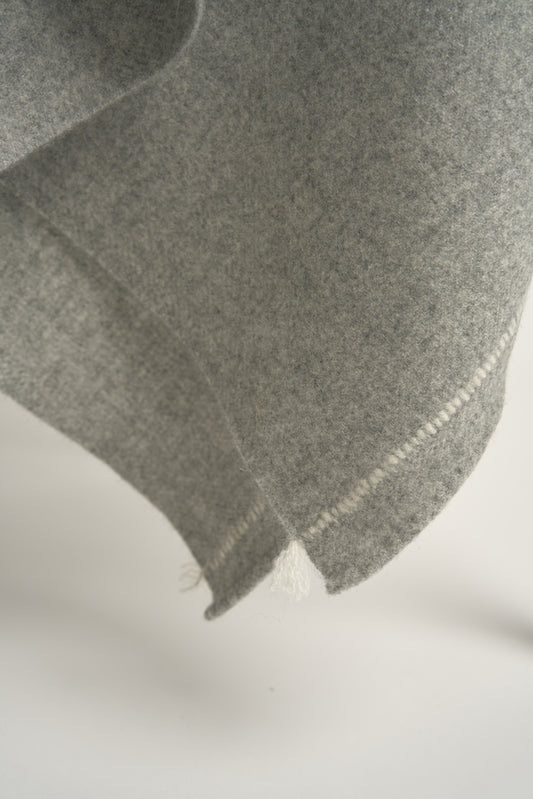 A soft grey throw with hand-rolled edges and a contrast color stitch line; draped over a chair