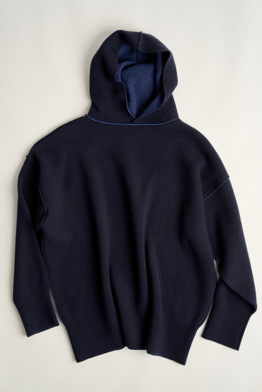 This image features a luxurious reversible blue cashmere hoodie, displayed against a neutral background to emphasize its design and color. The hoodie boasts a modern and minimalist look, with a soft and snug fit that promises comfort and style.