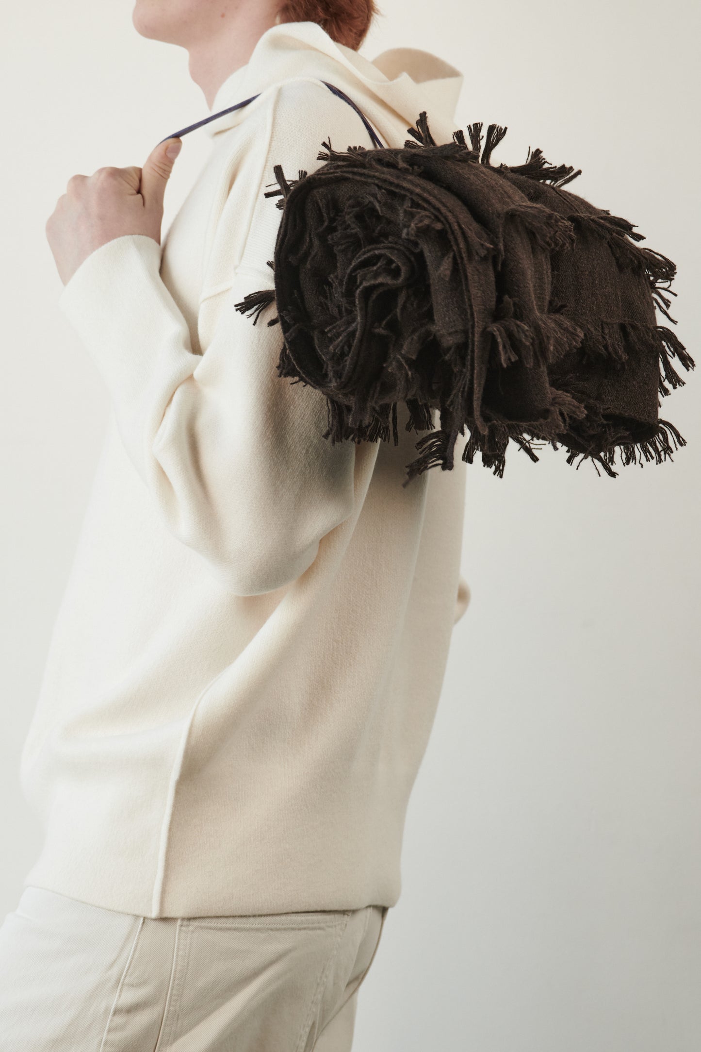 This image features a luxurious ivory cashmere hoodie, displayed against a neutral background to emphasize its design and color. The hoodie boasts a modern and minimalist look, with a soft and snug fit that promises comfort and style. Draped over the shoulder is a chocolate travel throw