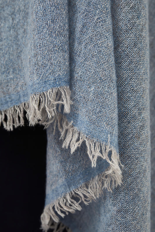 This image displays the Sera Shawl, a luxurious and elegant accessory crafted from the finest cashmere. The shawl features a subtle two-tone effect, achieved through a combination of different colors on the warp and weft, which enhances its sophisticated appeal.