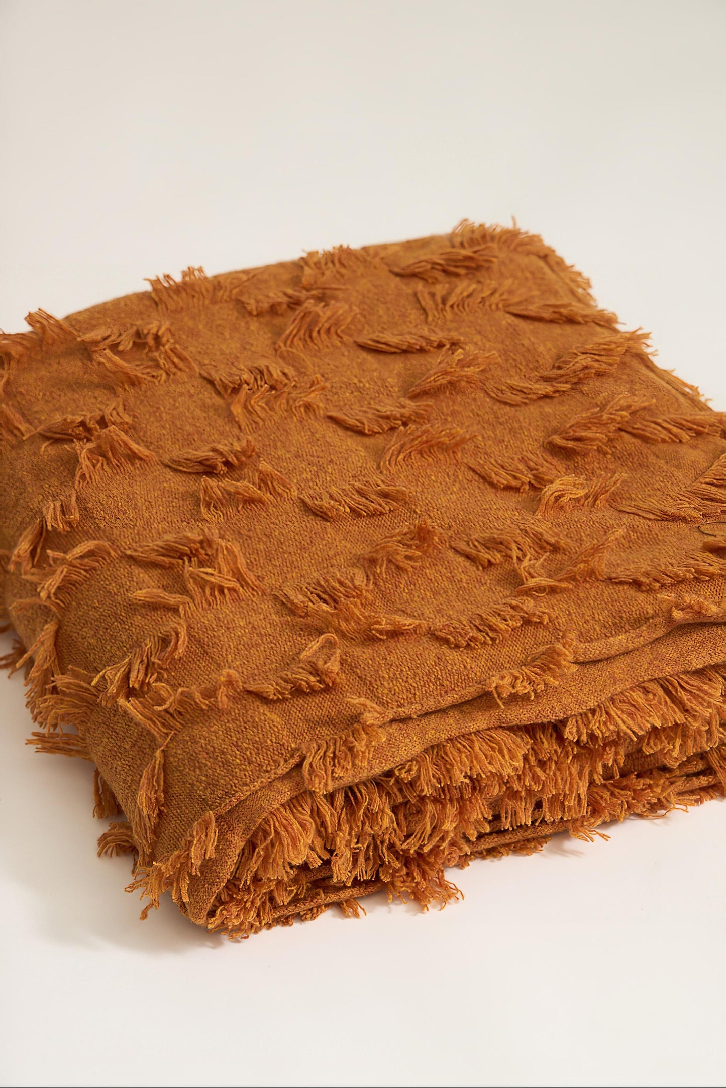 A honey bedspread with hand-cut fringe detail, draped over a chair.