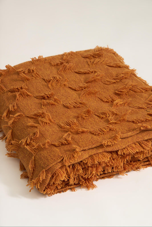 A honey bedspread with hand-cut fringe detail, draped over a chair.
