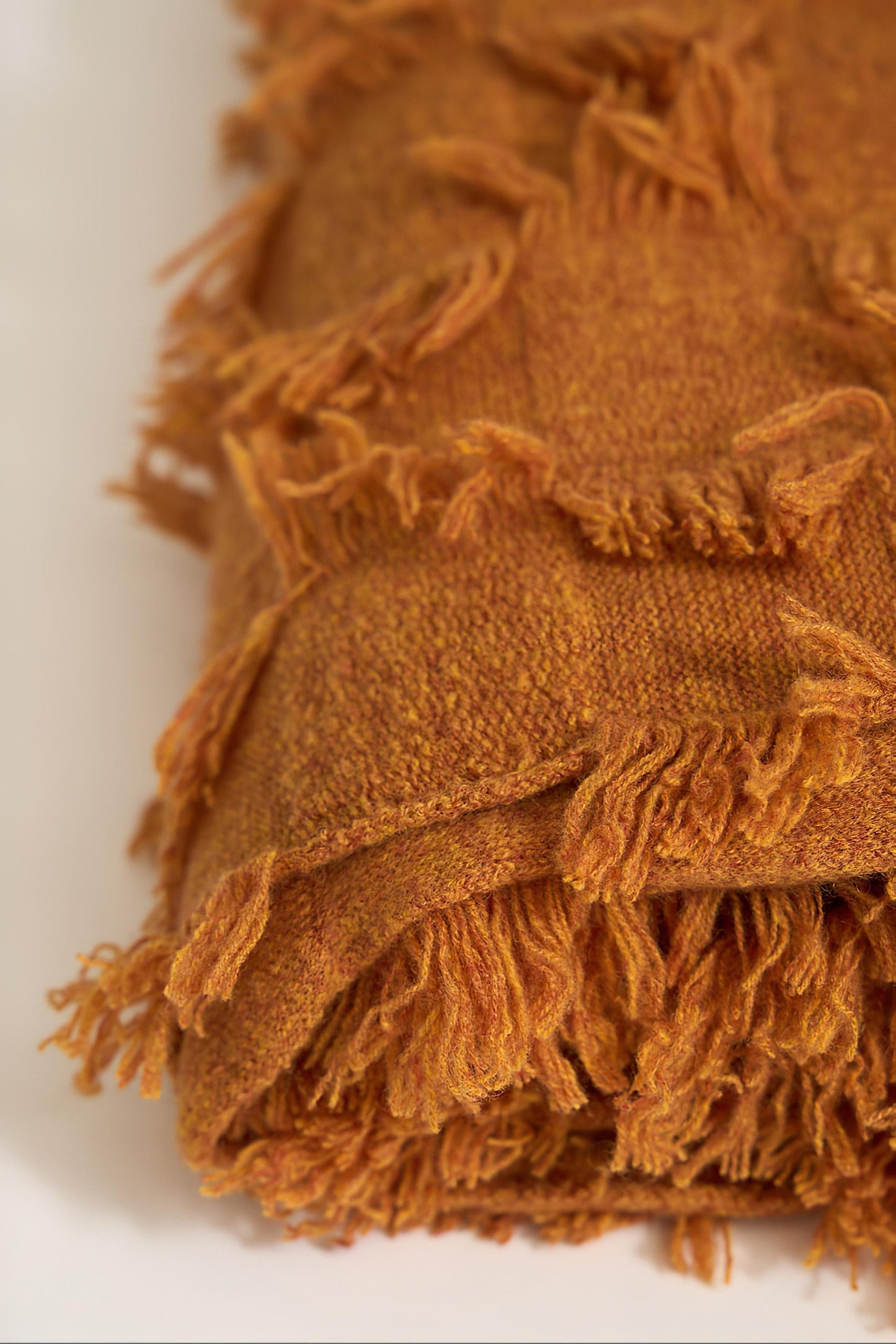 A honey bedspread with hand-cut fringe detail. Folded neatly on a white background.