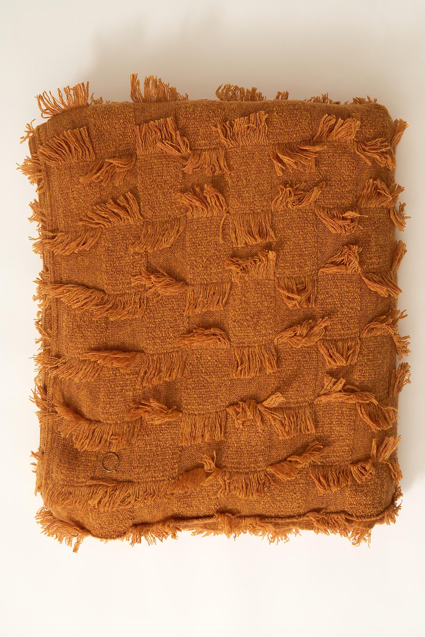 A honey bedspread with hand-cut fringe detail. Folded neatly on a white background.