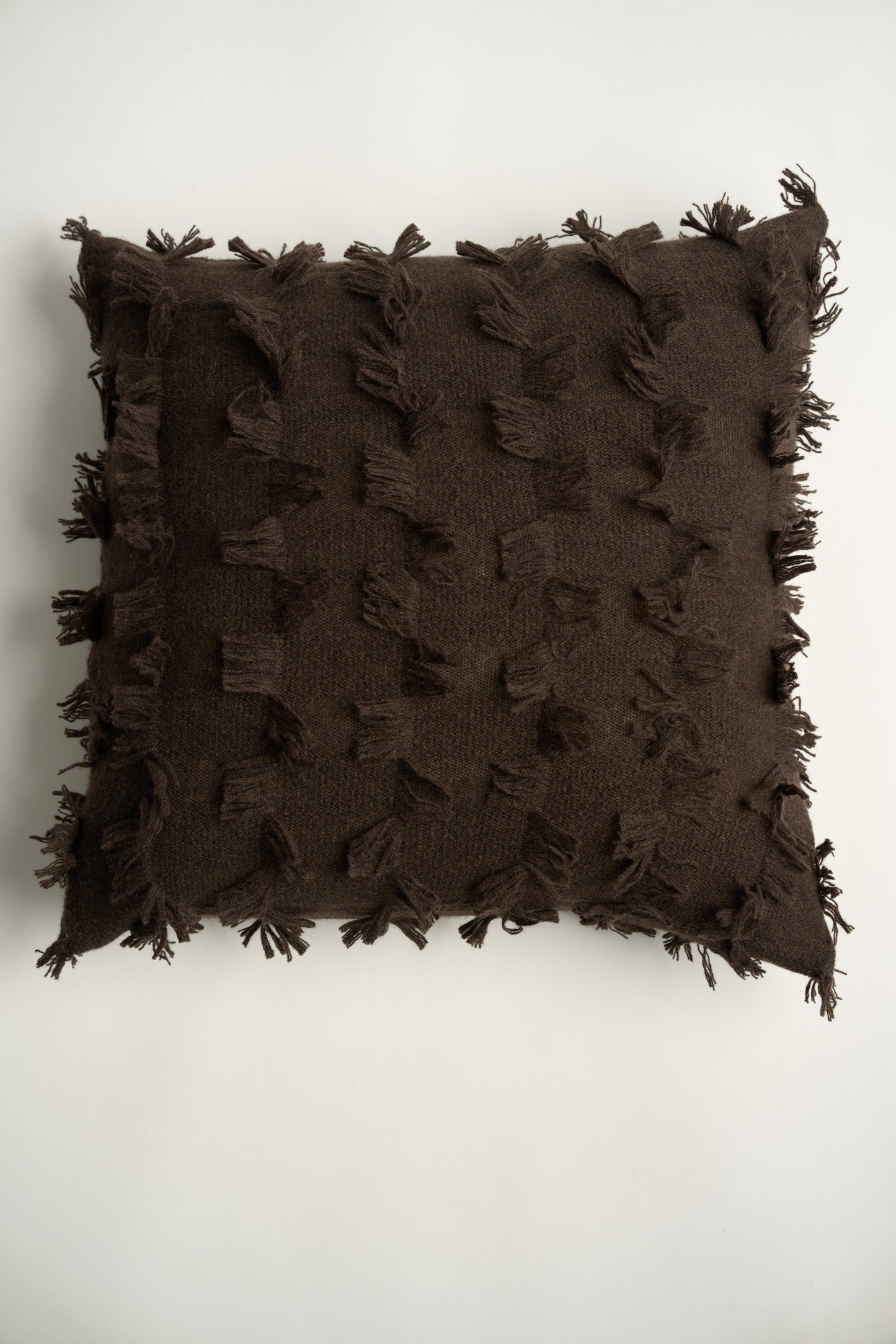 This image displays the Seren Cushion Cover, designed to bring a touch of serene elegance to any interior setting. The cushion cover features a distinct hand-cut fringe detail that adds a textured and dynamic touch.