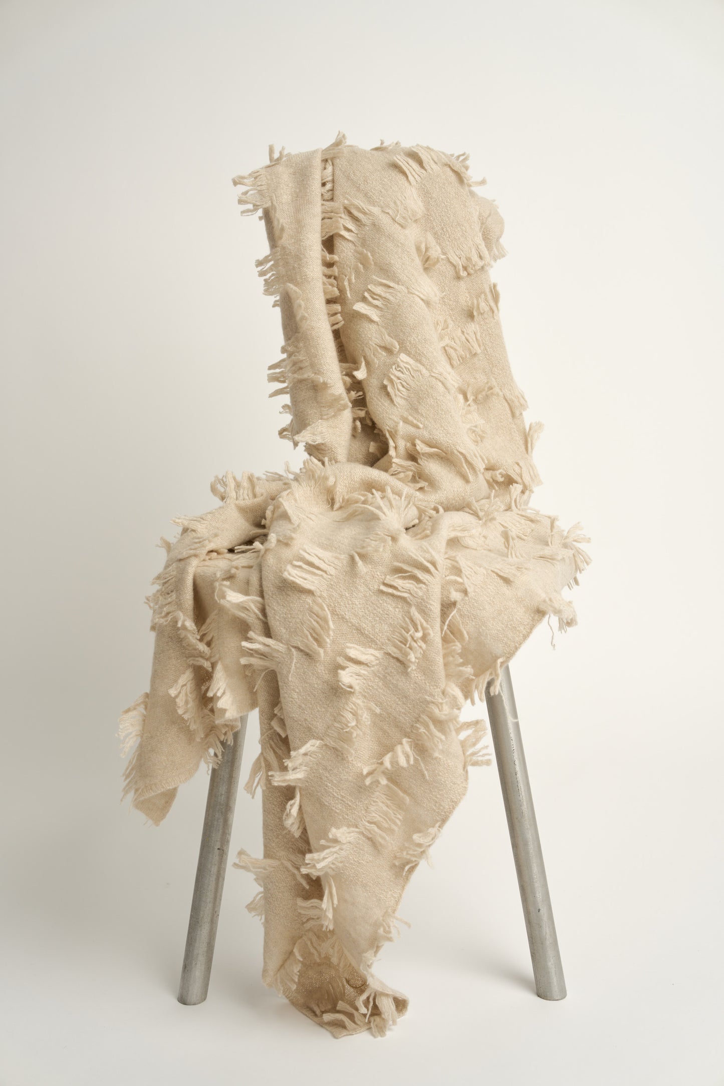 This image displays the Seren Throw, a luxurious cashmere knitted throw featuring a distinctive hand-cut fringe detail. The throw is presented in a bright, warm beige color, enhancing its elegant and sophisticated appearance.