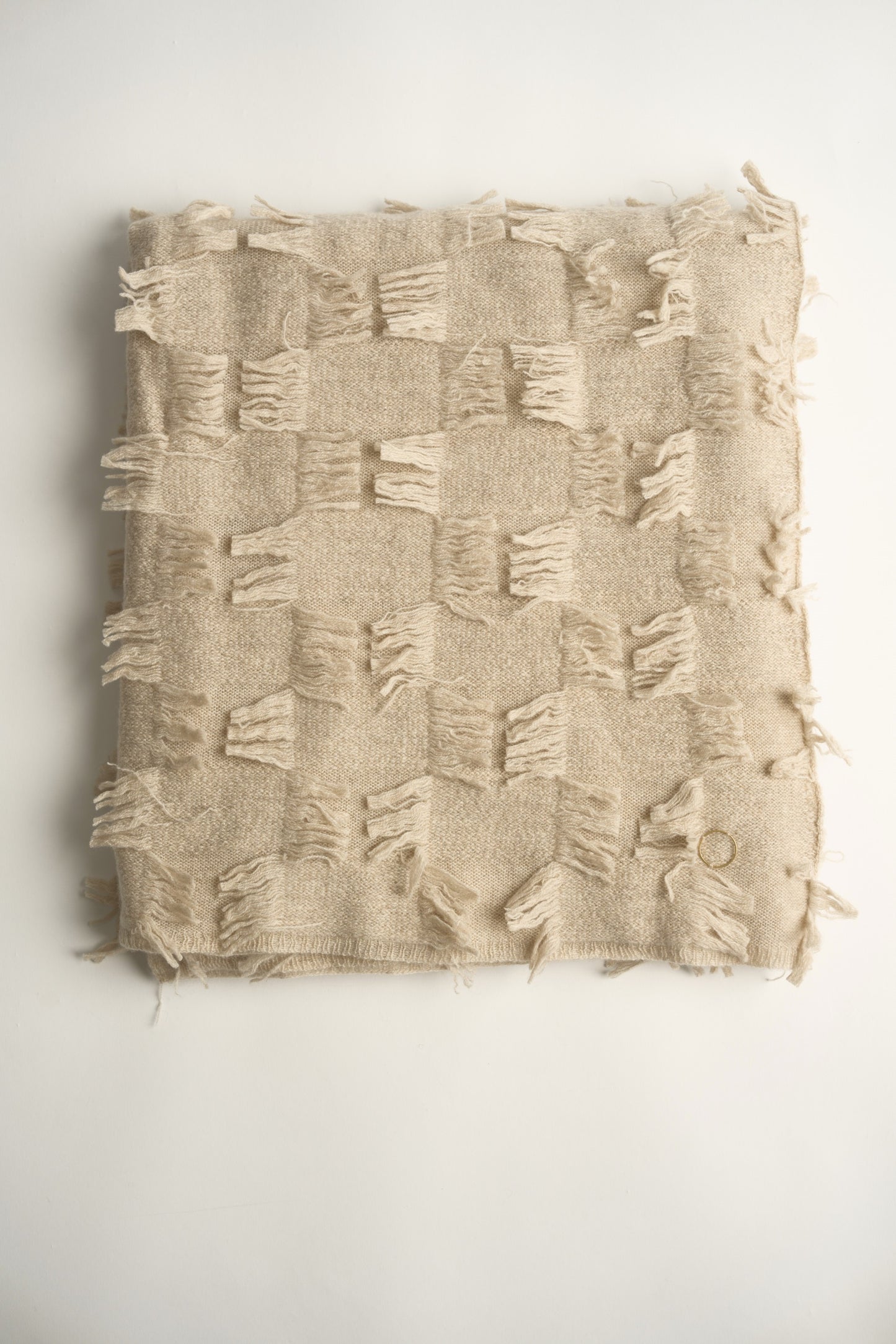 This image displays the Seren Throw, a luxurious cashmere knitted throw featuring a distinctive hand-cut fringe detail. The throw is presented in a bright, warm beige color, enhancing its elegant and sophisticated appearance.