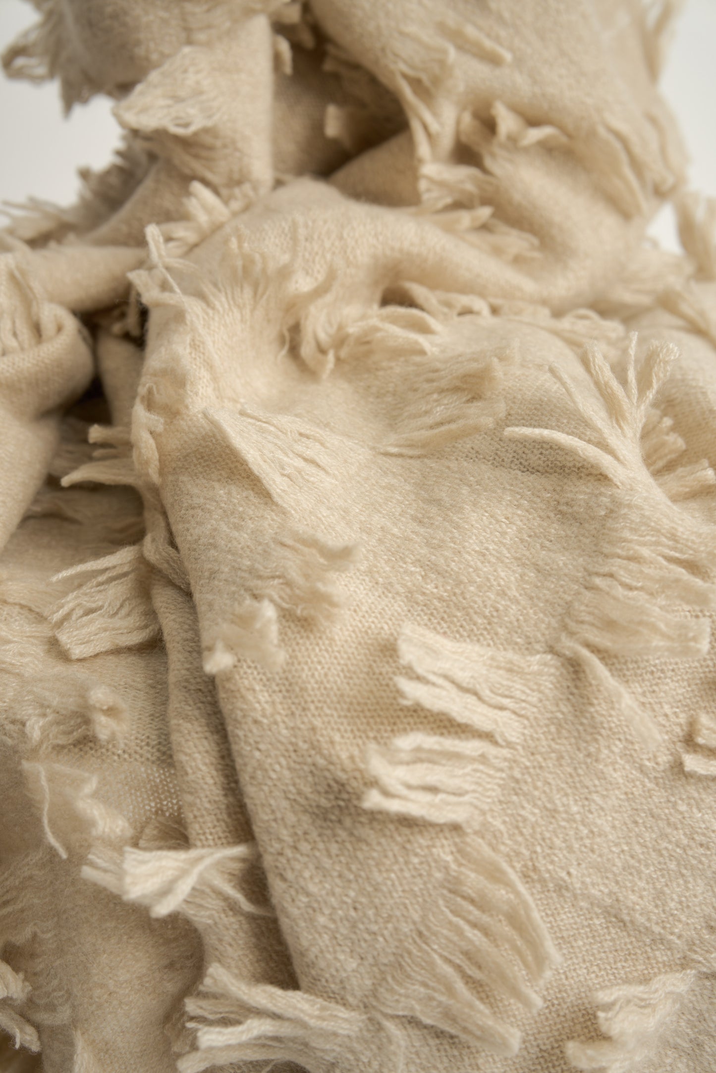 This image displays the Seren Throw, a luxurious cashmere knitted throw featuring a distinctive hand-cut fringe detail. The throw is presented in a bright, warm beige color, enhancing its elegant and sophisticated appearance.