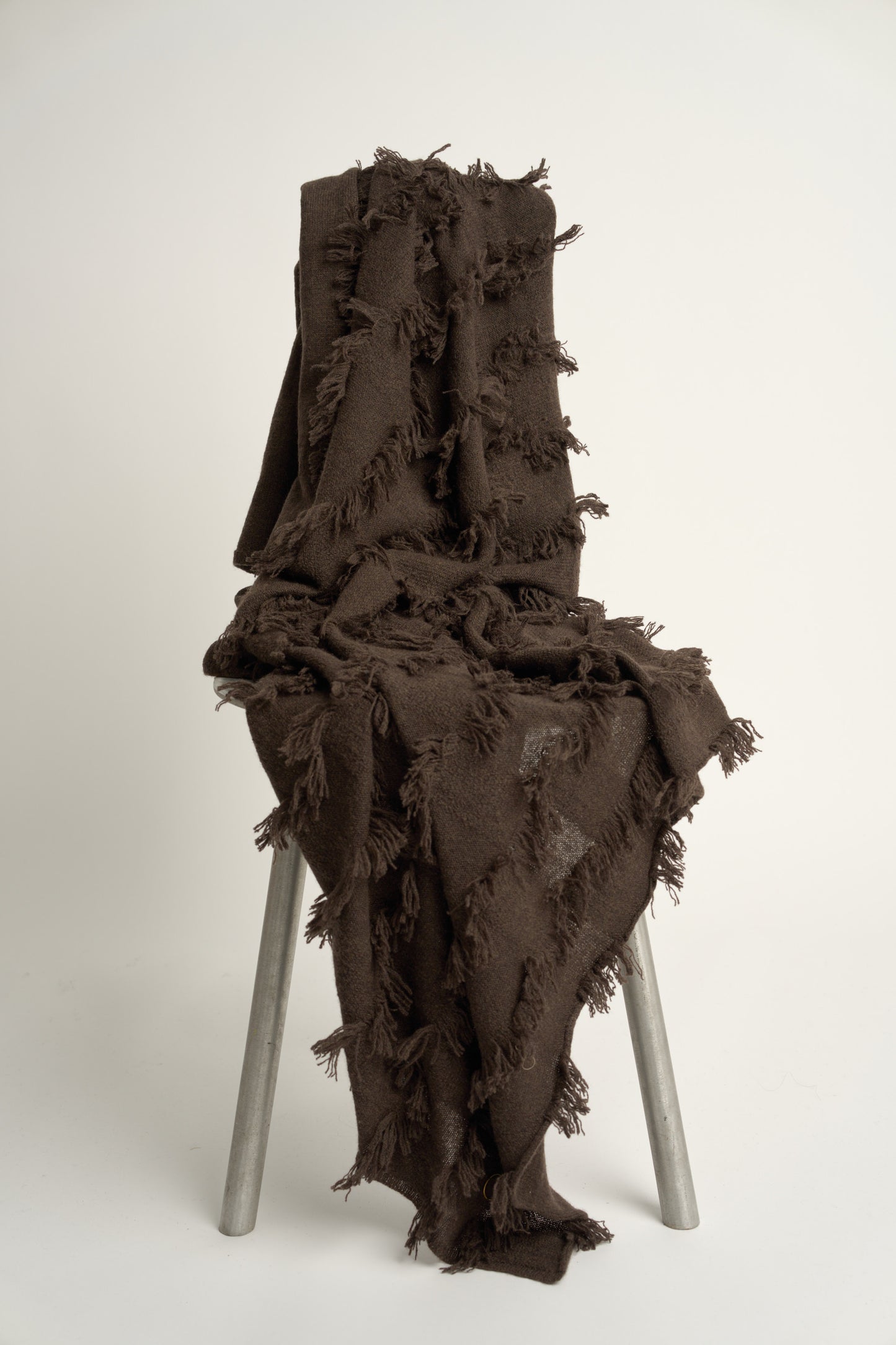 This image displays the Seren Throw, a luxurious cashmere knitted throw featuring a distinctive hand-cut fringe detail. The throw is presented in a deep, rich brown color, enhancing its elegant and sophisticated appearance.