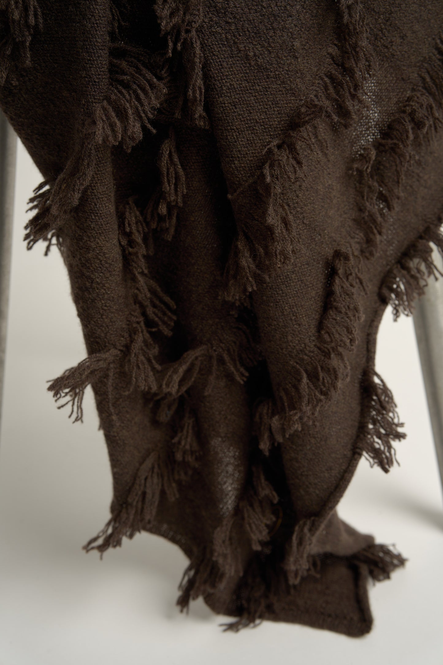 This image displays the Seren Throw, a luxurious cashmere knitted throw featuring a distinctive hand-cut fringe detail. The throw is presented in a deep, rich brown color, enhancing its elegant and sophisticated appearance.