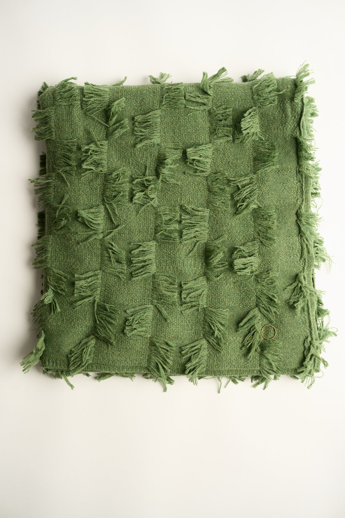 This image displays the Seren Throw, a luxurious cashmere knitted throw featuring a distinctive hand-cut fringe detail. The throw is presented in a natural, embracing green color, enhancing its elegant and sophisticated appearance.