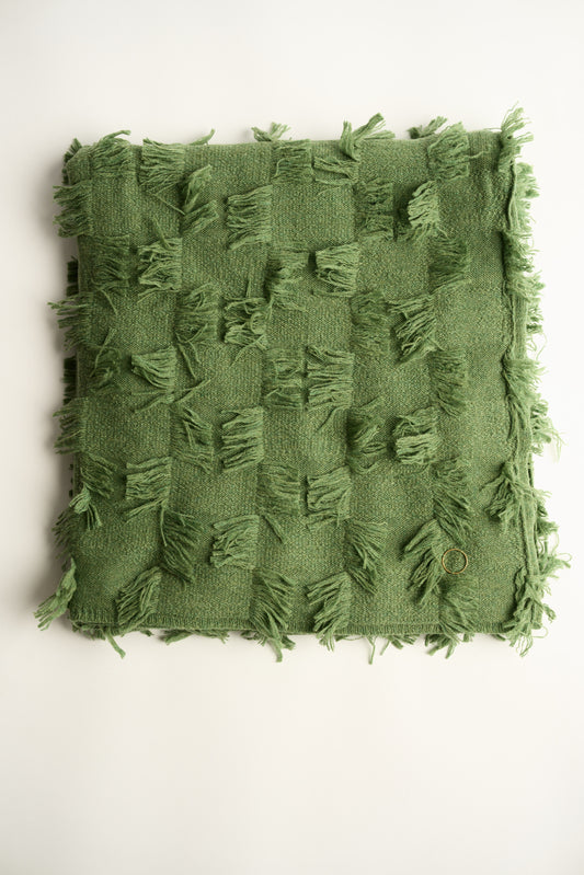 This image displays the Seren Throw, a luxurious cashmere knitted throw featuring a distinctive hand-cut fringe detail. The throw is presented in a natural, embracing green color, enhancing its elegant and sophisticated appearance.