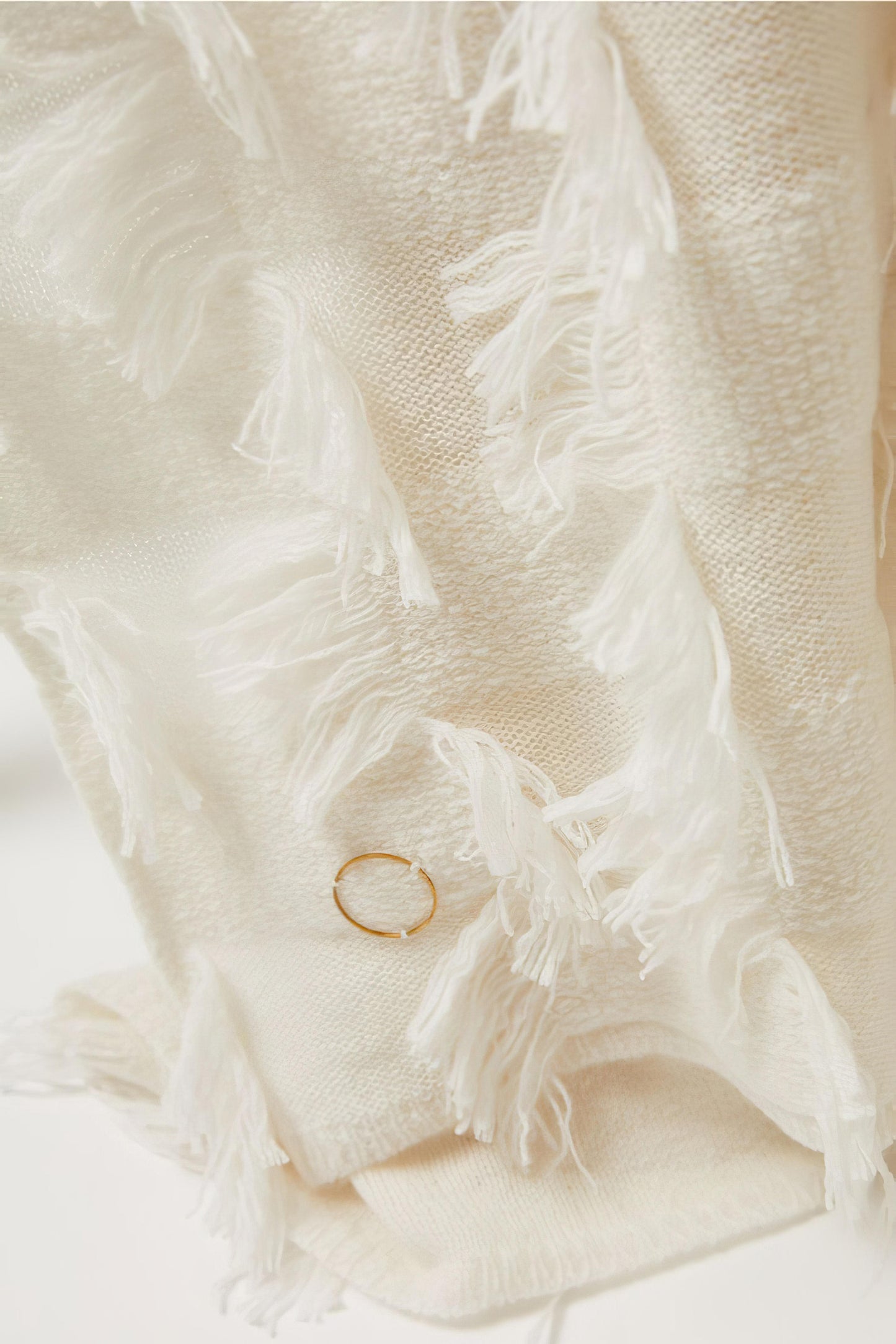 An ivory bedspread with hand-cut fringe detail, draped over a chair.