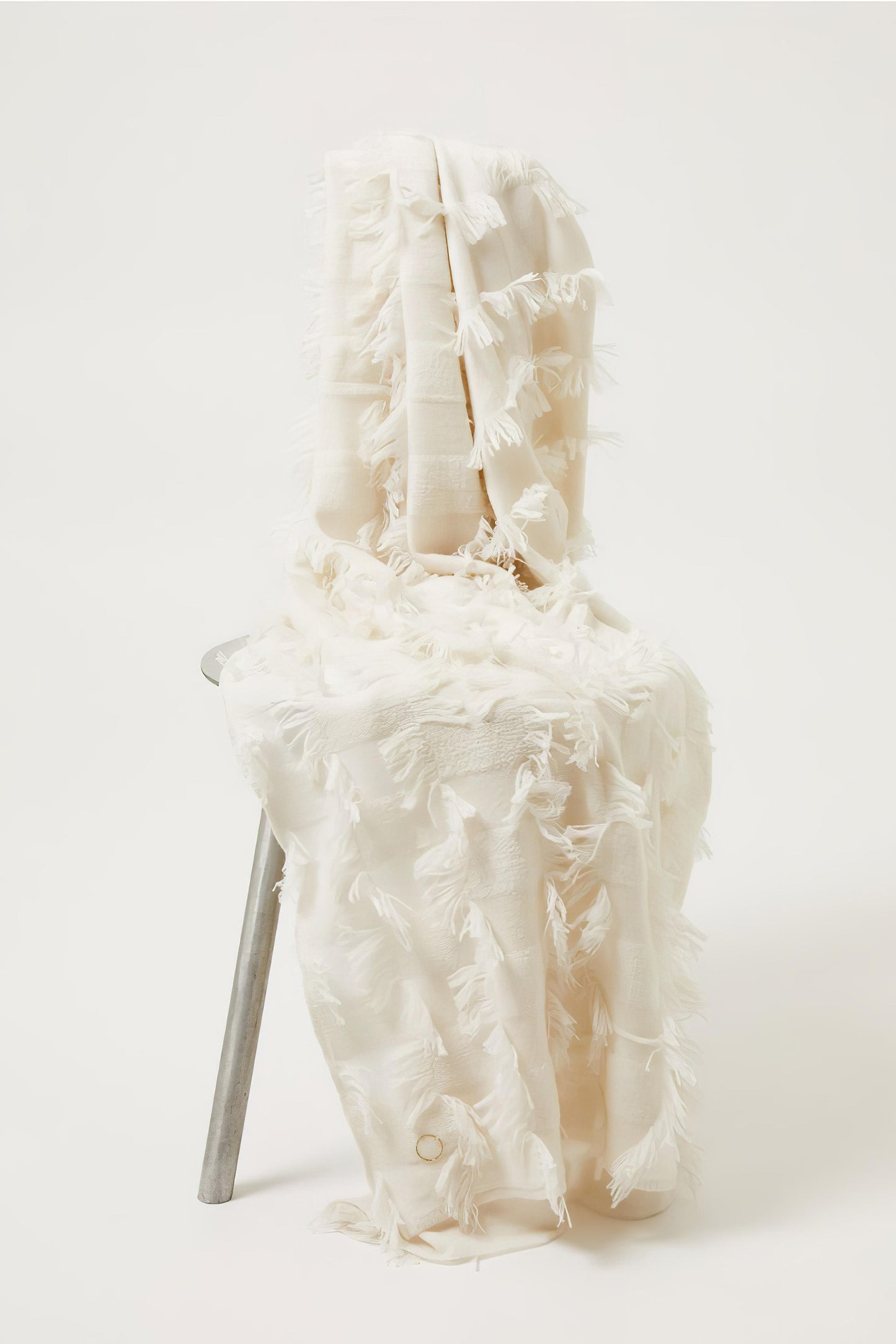 This image displays the Seren Throw, a luxurious cashmere knitted throw featuring a distinctive hand-cut fringe detail. The throw is presented in a light, bright ivory color, enhancing its elegant and sophisticated appearance.
