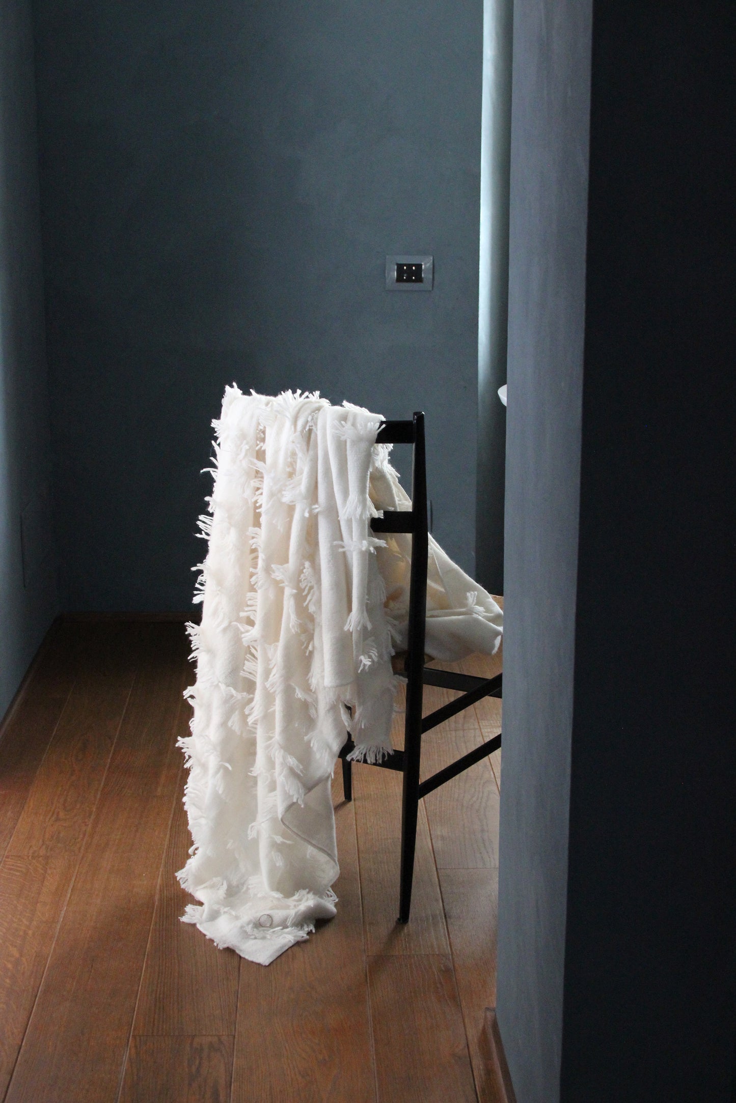 This image displays the Seren Throw, a luxurious cashmere knitting throw featuring a distinctive hand-cut fringe detail. The throw is presented in a light, bright ivory color, enhancing its elegant and sophisticated appearance.