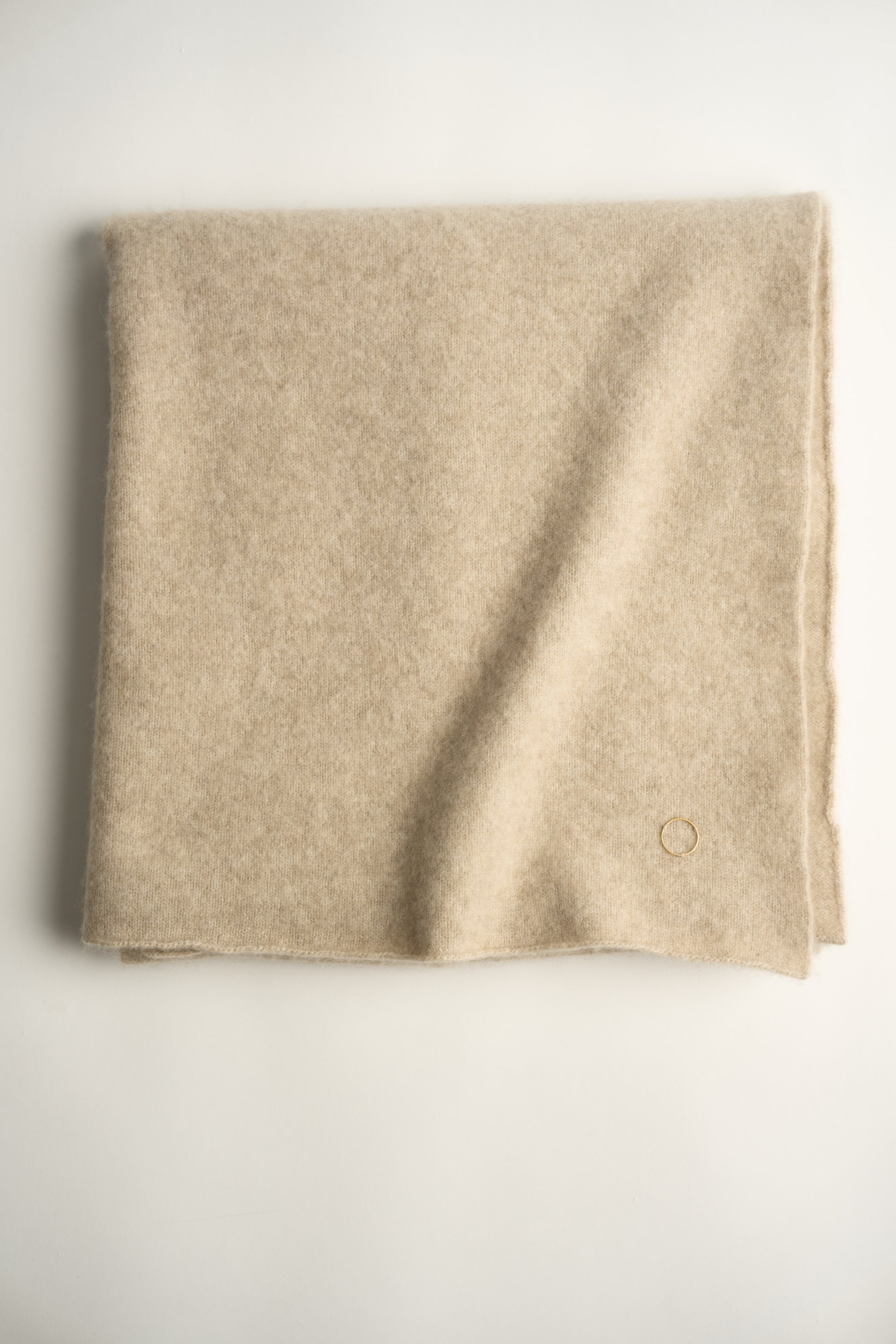 This image displays the "Silence Throw," a luxurious knitted felted throw that offers both warmth and a soft texture. Its unique design, characterized by a subtle, uniform texture and a small, discreet circle detail in the corner, enhances its plush appeal.