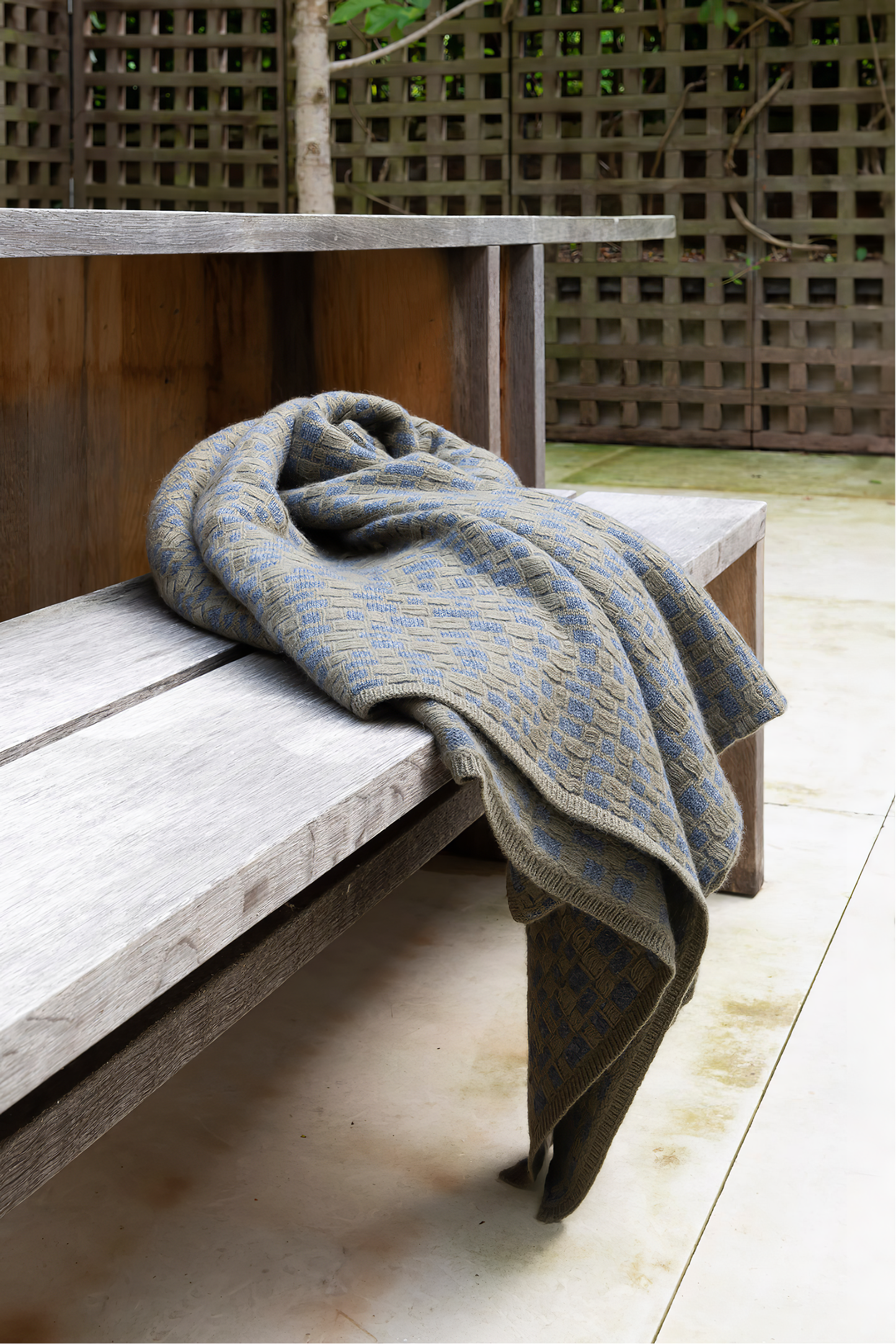 This image features the "stone throw in moss & slate," a luxurious and meticulously crafted cashmere throw. The throw displays an elegant pattern that resembles the texture of slate floors, complemented by bands of yarn in varying lengths that add a subtle yet dynamic visual appeal.