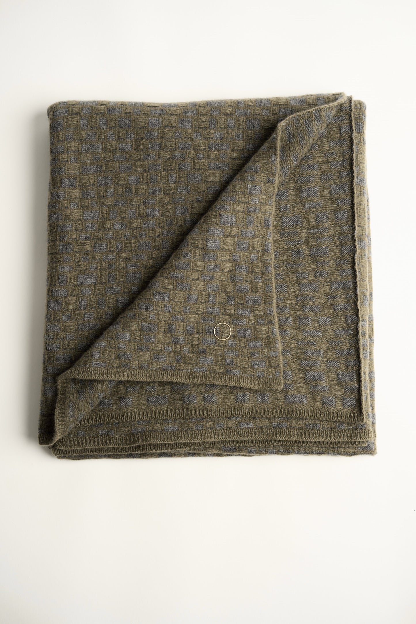This image features the "stone throw in moss & slate," a luxurious and meticulously crafted cashmere throw. The throw displays an elegant pattern that resembles the texture of slate floors, complemented by bands of yarn in varying lengths that add a subtle yet dynamic visual appeal.