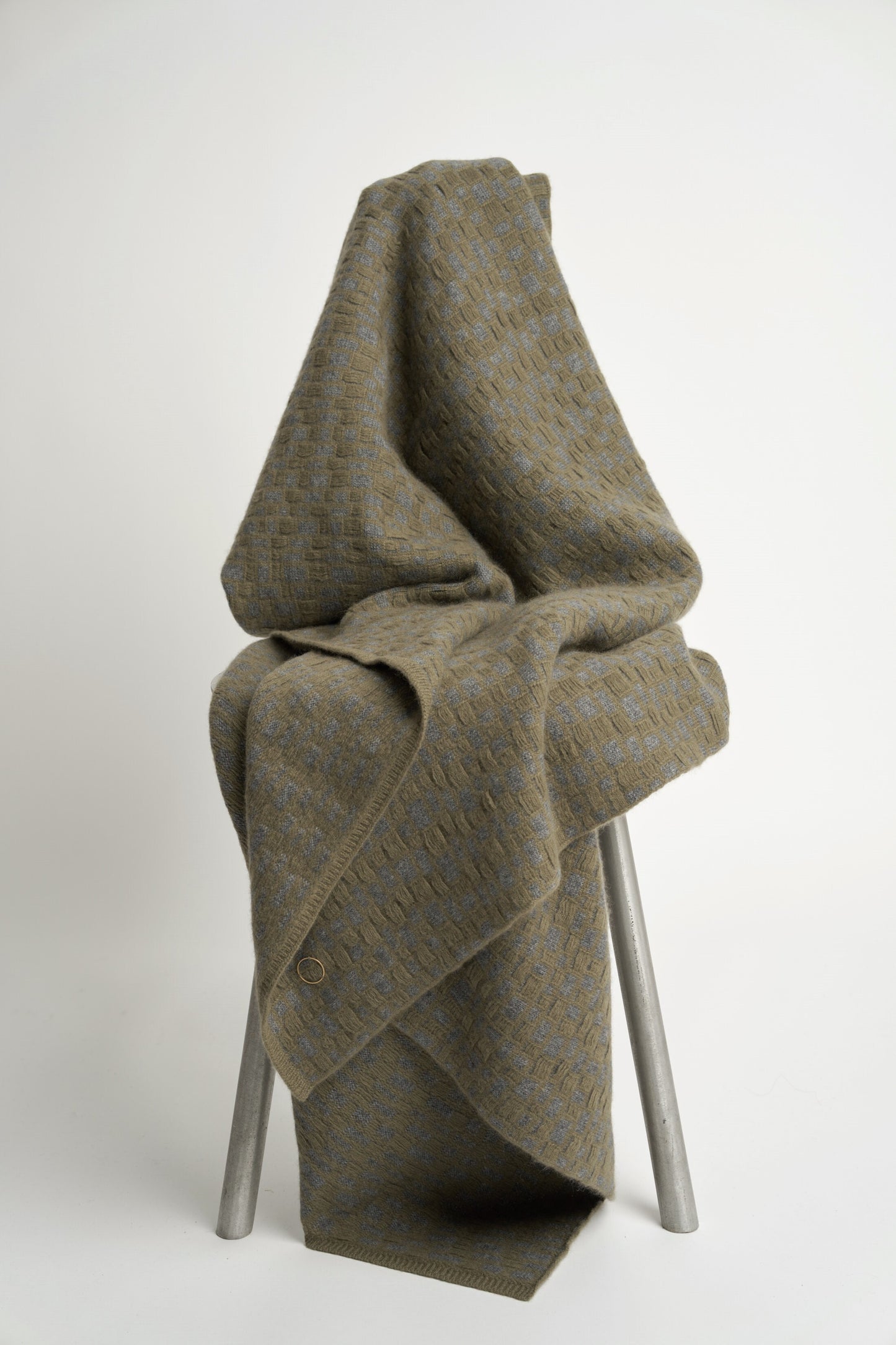 This image features the "stone throw in moss & slate," a luxurious and meticulously crafted cashmere throw. The throw displays an elegant pattern that resembles the texture of slate floors, complemented by bands of yarn in varying lengths that add a subtle yet dynamic visual appeal.