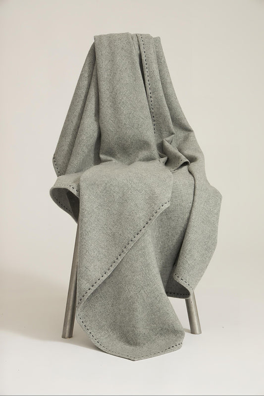 A soft grey Suono throw with hand-stitched edges, folded over a chair and displayed on a white background.