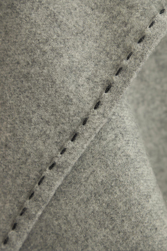 A soft grey Suono throw with hand-stitched edges, folded over a chair and displayed on a white background.