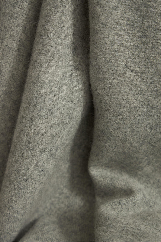 A soft grey Suono throw with hand-stitched edges, folded over a chair and displayed on a white background.