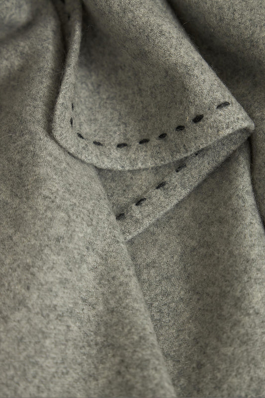 A soft grey Suono throw with hand-stitched edges, folded over a chair and displayed on a white background.