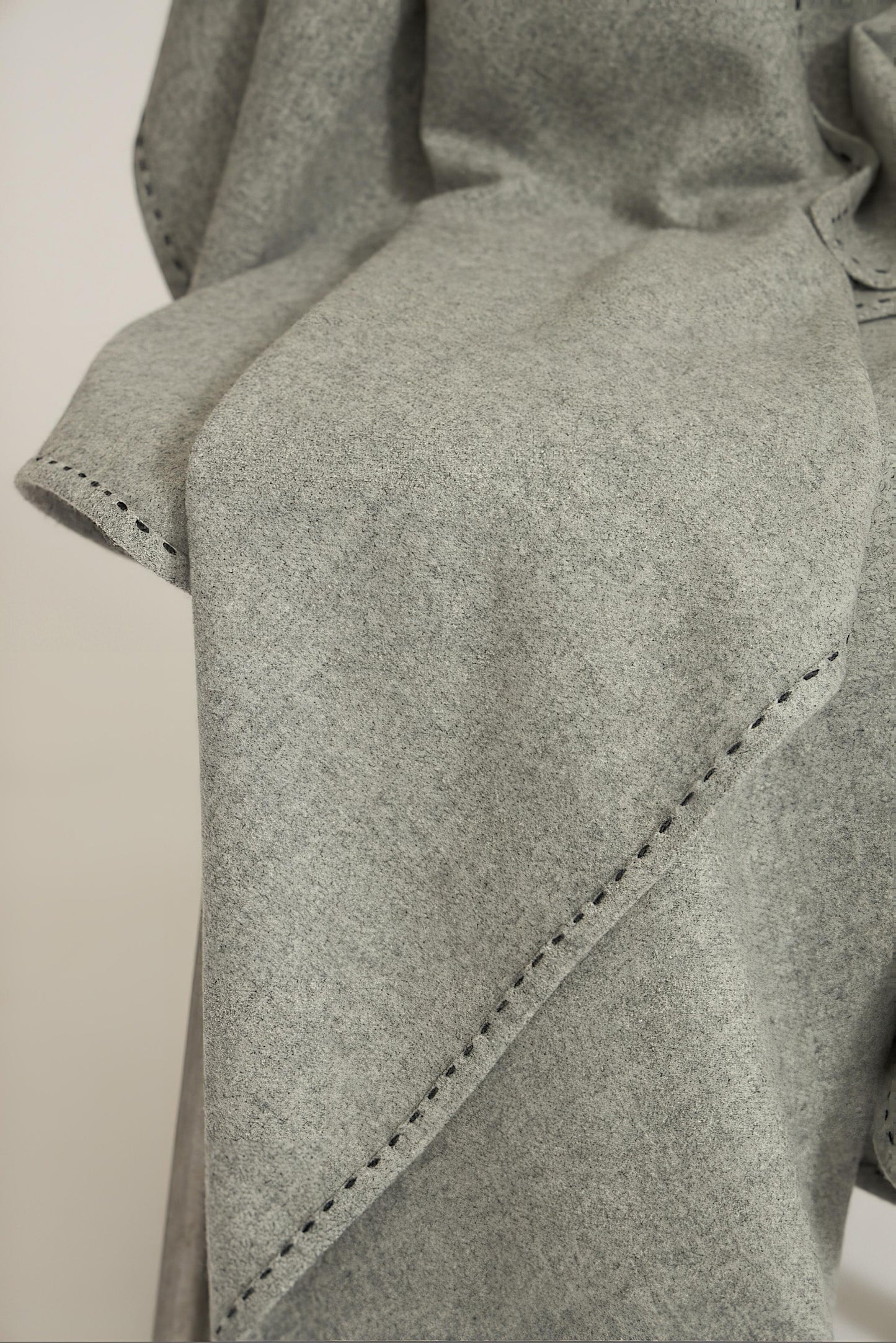 A soft grey Suono throw with hand-stitched edges, folded over a chair and displayed on a white background.