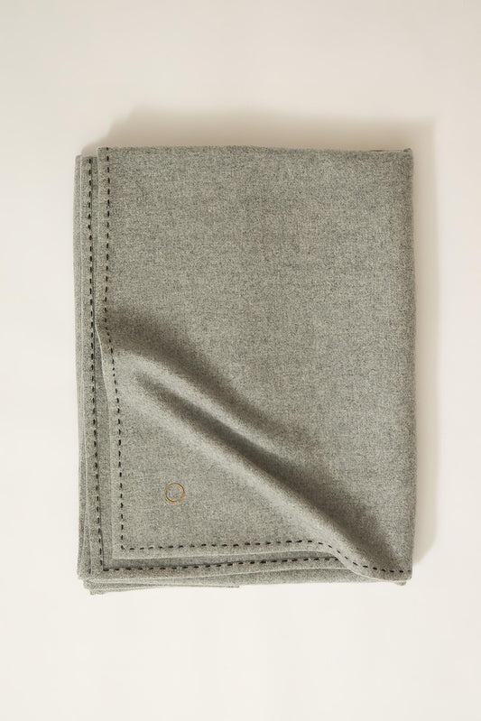 A soft grey Suono throw with hand-stitched edges, folded over a chair and displayed on a white background.