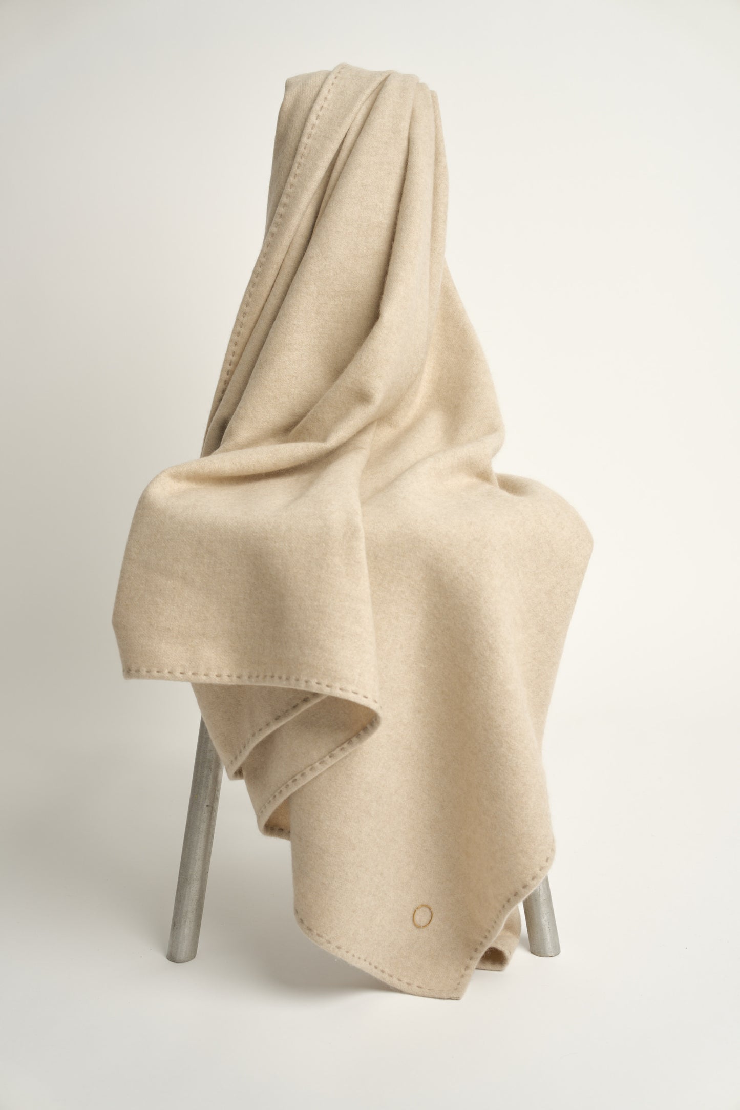 A beige Suono throw with hand-stitched edges, folded over a chair and displayed on a white background.