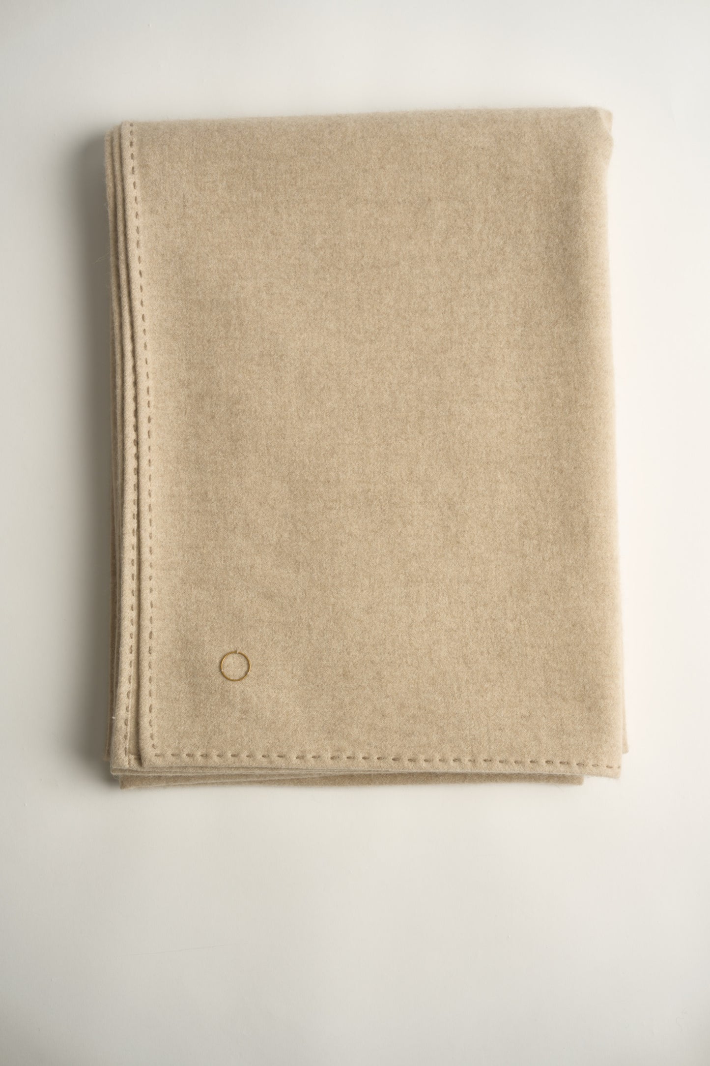 A folded beige Suono throw with hand-stitched edges, folded over a chair and displayed on a white background.