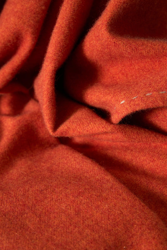 A fire Suono throw with hand-stitched edges, folded over a chair and displayed on a white background.