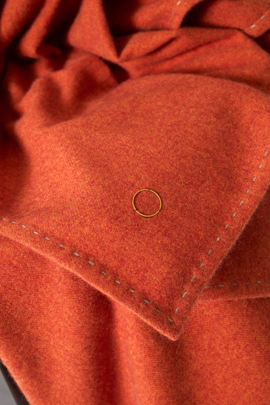 A fire Suono throw with hand-stitched edges, folded over a chair and displayed on a white background.