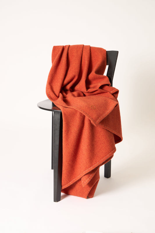A fire Suono throw with hand-stitched edges, folded over a chair and displayed on a white background.