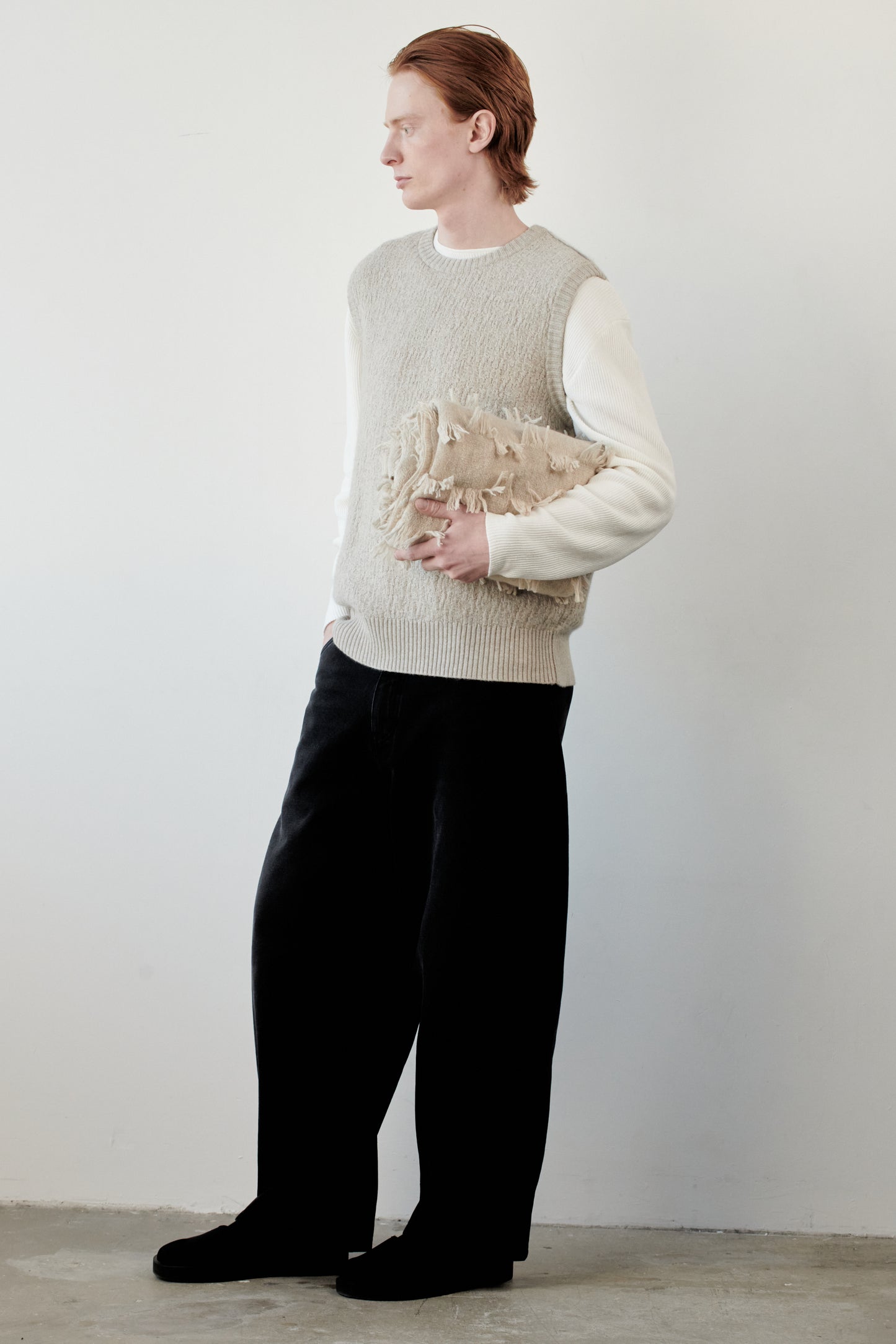 This image features the Terra Top, a stylish knitted texture vest crafted from 100% cashmere, providing an unmatched softness and warmth. The model is seen wearing the vest in a layering style over a cream-colored sweater, paired with dark trousers, showcasing the vest's sophisticated and subtle textured design.