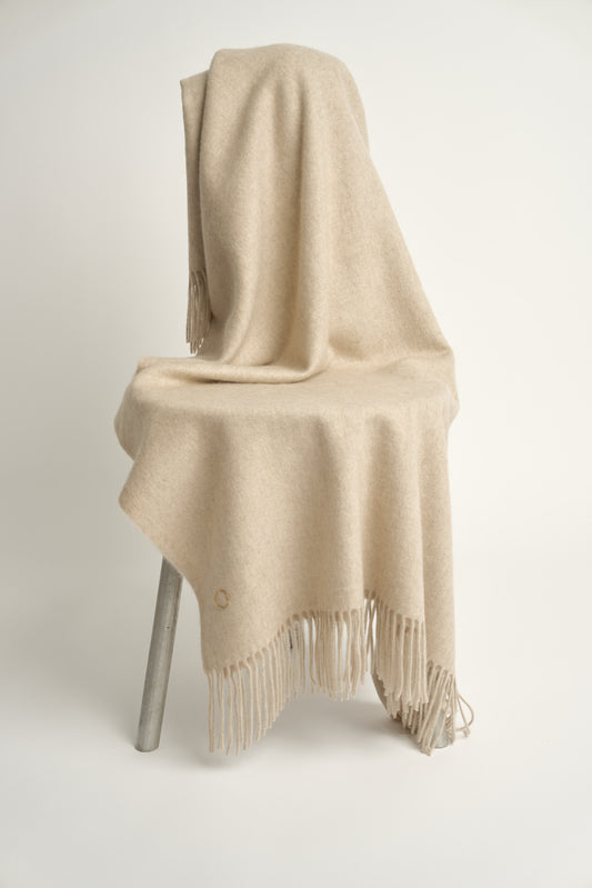 A beige cashmere throw with fringes at the top and bottom edges, displayed on a chair