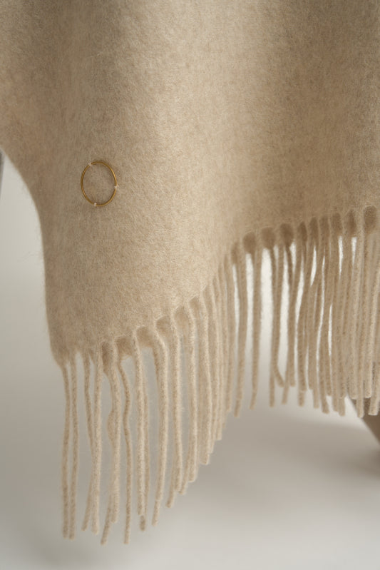 A beige cashmere throw with fringes at the top and bottom edges, displayed on a chair
