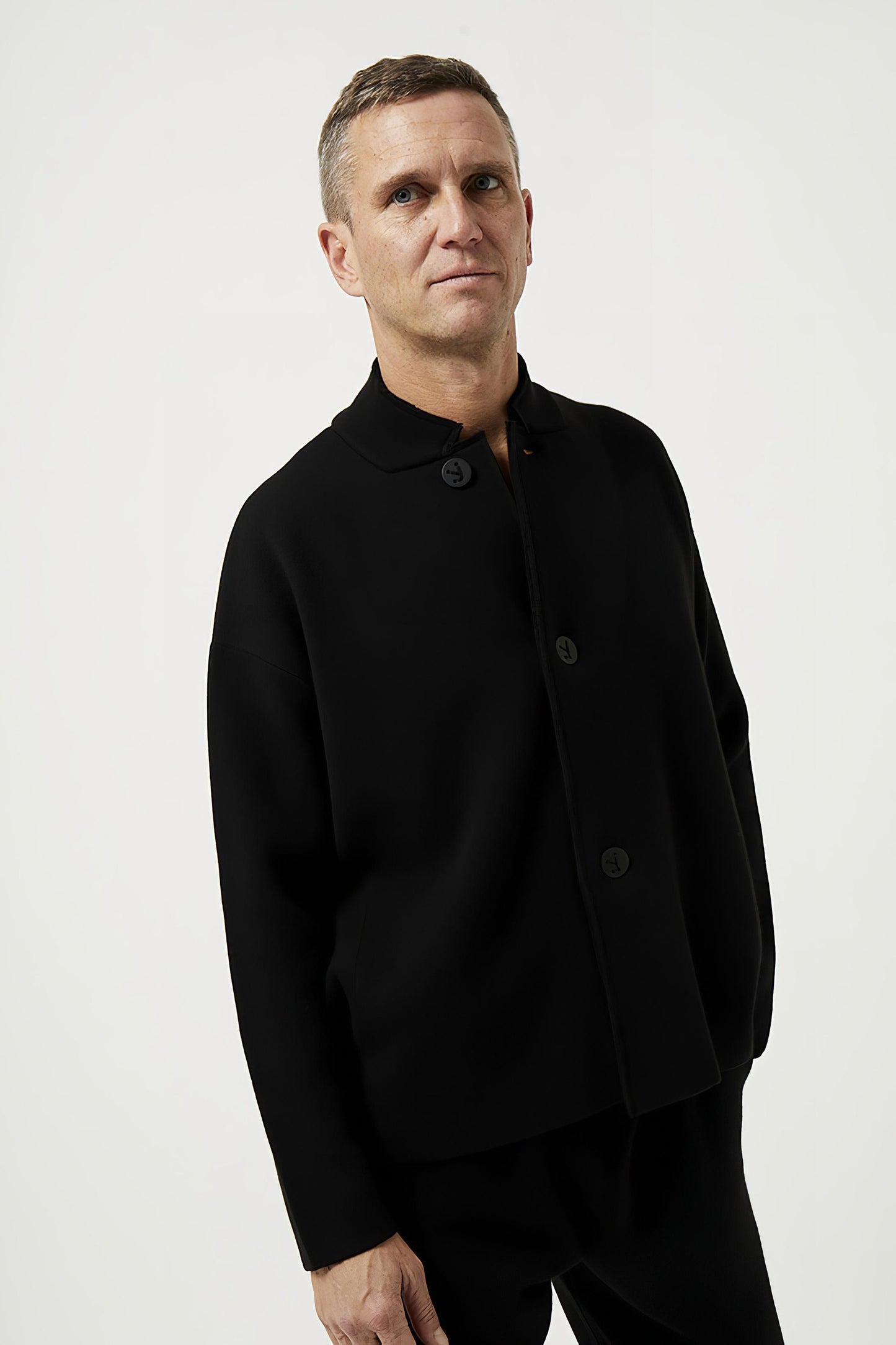 This image features a model wearing the Wind Jacket from Oyuna's core collection. The jacket is designed with a relaxed-fit and showcases a sophisticated look with its stand-up collar and welt pockets.