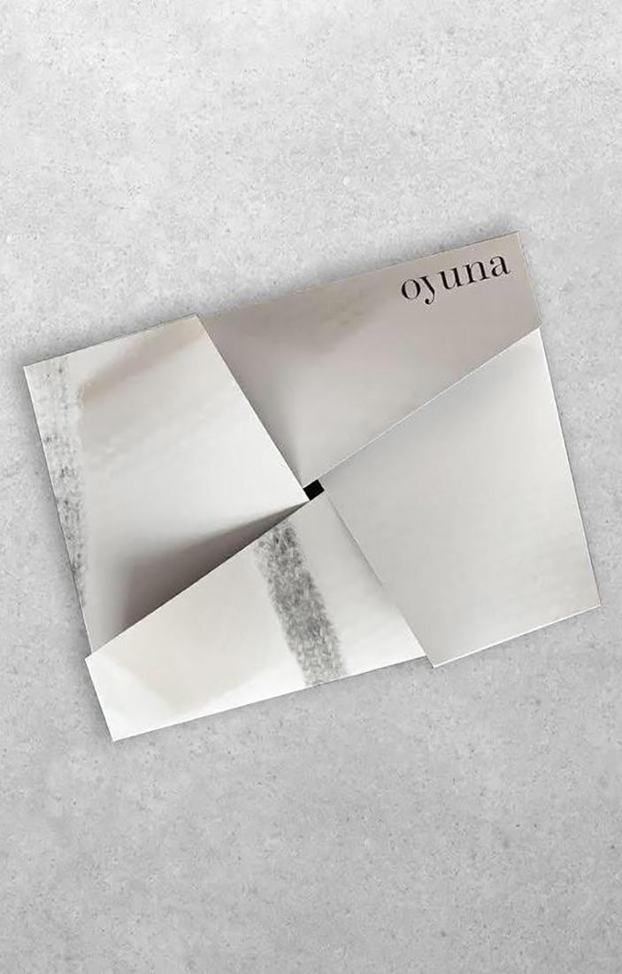 This image features a sleek and elegant Oyuna gift card, presented in a beautifully crafted origami envelope. The envelope, shown in a pale grey hue, displays a minimalist design with a distinctive crease in the center, revealing a personalized message that reads "Oyuna.