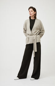 Person wearing Axomi wrap jacket in cashmere in colour Feather.  A relaxed fit jacket with statement sleeves and removable tie belt in cashmere. 