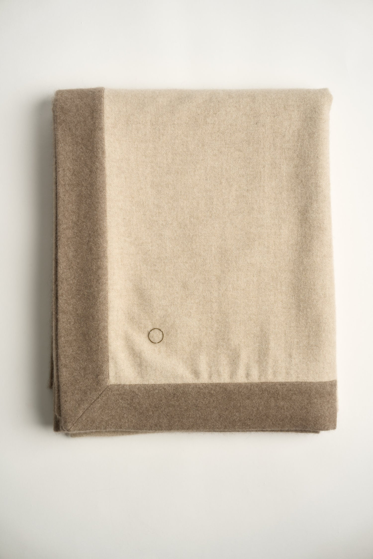 A beige and taupe etra throw blanket with a subtle pattern, neatly folded.