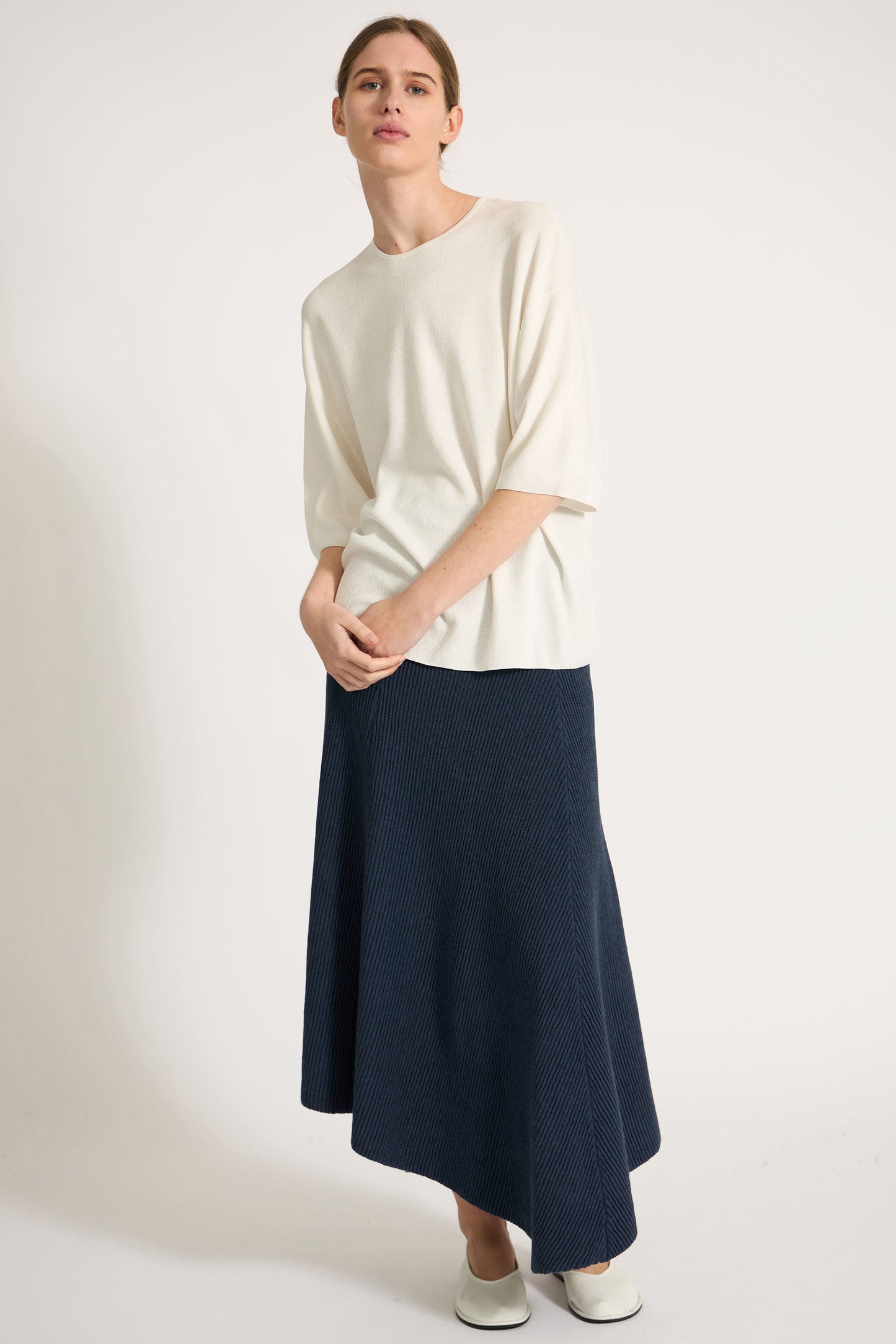 Person wearing an ivory top and navy skirt on a plain background