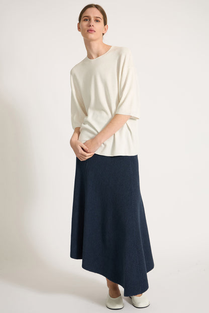Person wearing an ivory top and navy skirt on a plain background