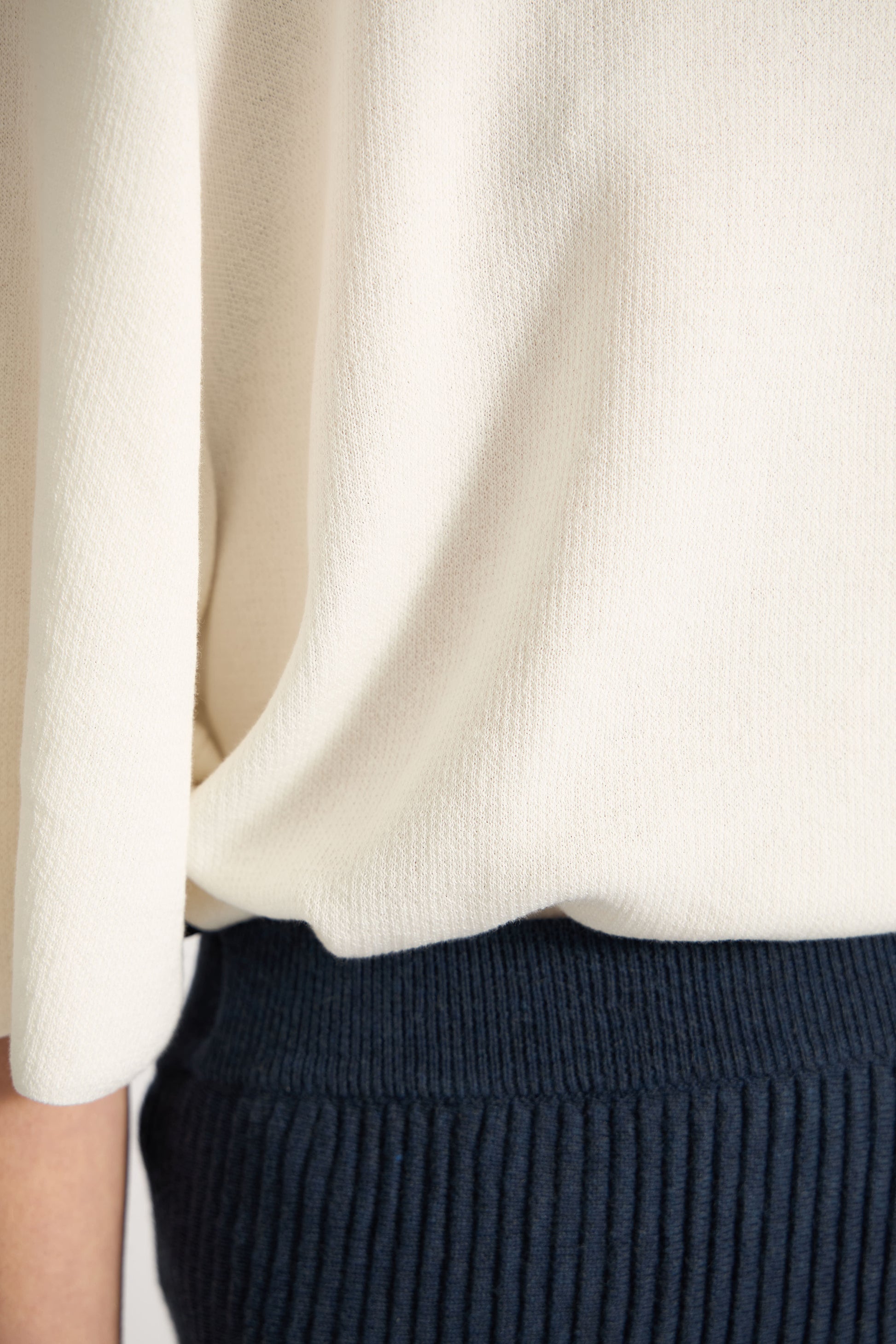 Close-up of a person wearing an ivory top and navy skirt.