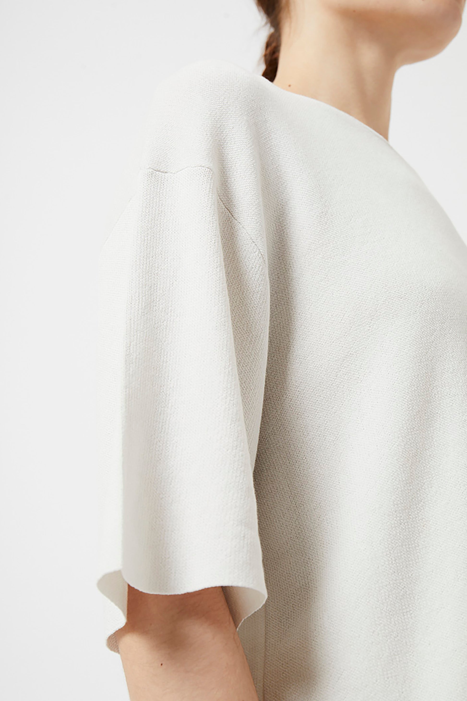 Close-up of a person wearing an ivory top with a plain background