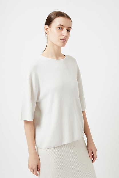 Woman wearing an ivory top against a plain background