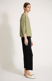 Woman wearing Sabi cotton sweater with dropped shoulders and cropped sleeves in colour Fern. 